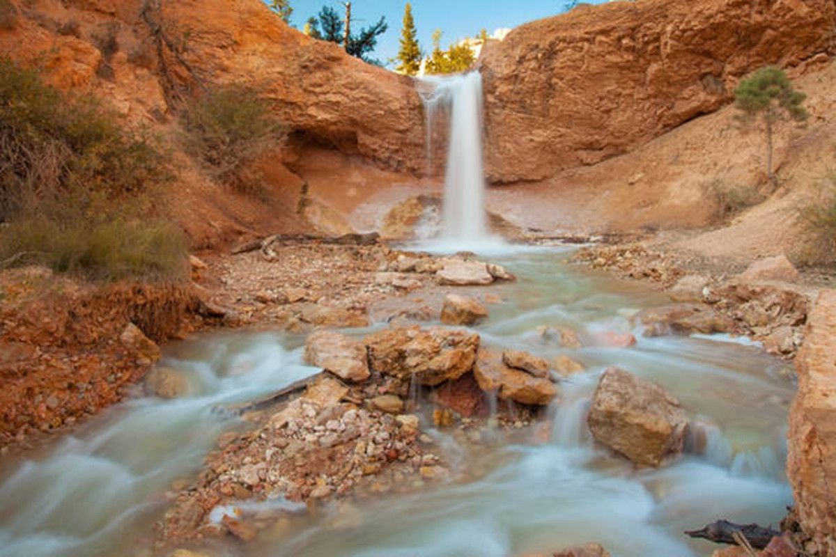 Une cascade dans un canyon rocheux, où une eau claire s’écoule sur les rochers.