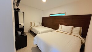 Ein Hotelzimmer mit zwei Einzelbetten, einem dunklen Holzkopfstück, einem kleinen Schreibtisch mit Spiegel und einer Nachttischlampe.
