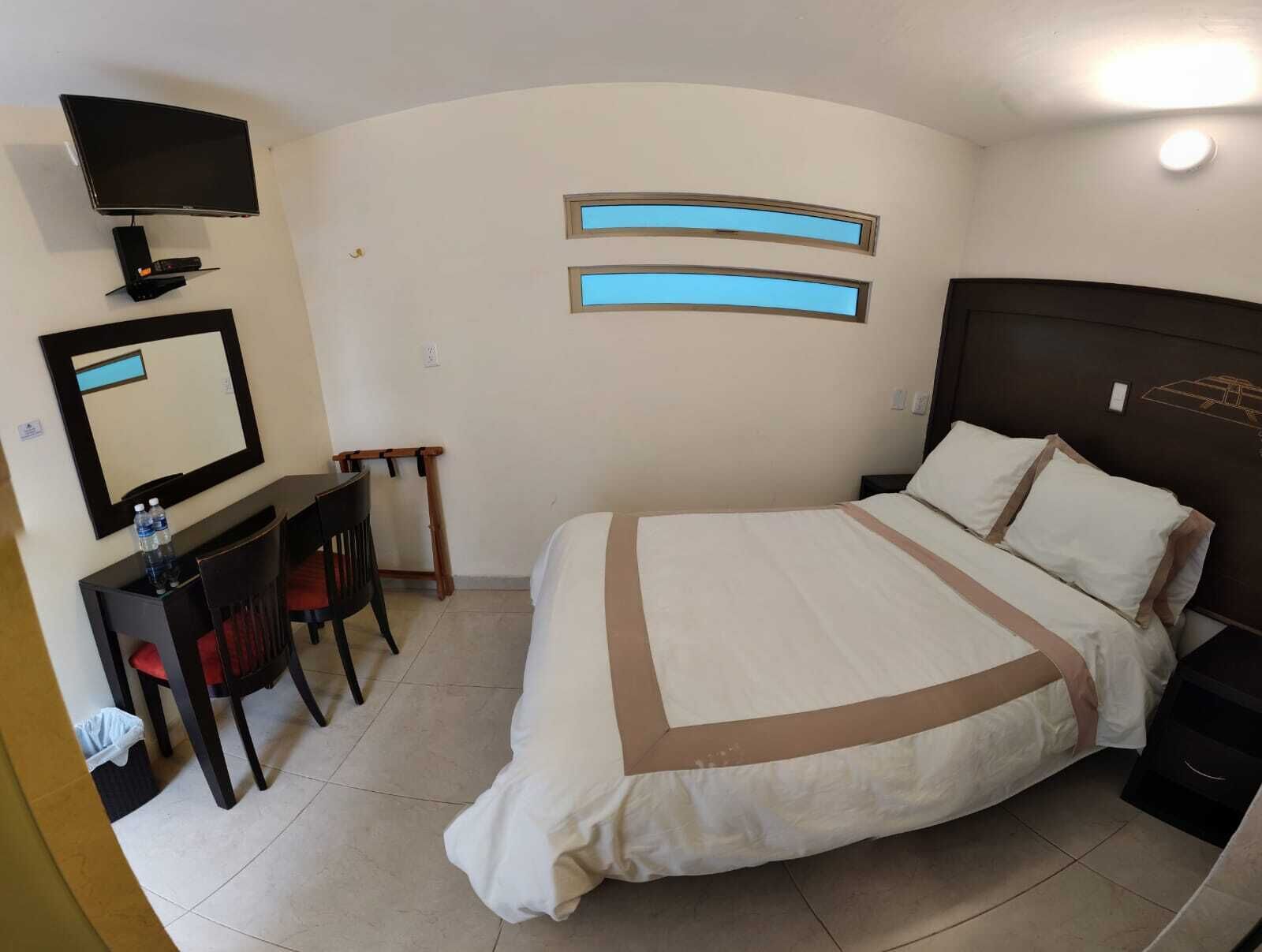 Una habitación de hotel con cama, escritorio, silla, televisor y dos ventanas.