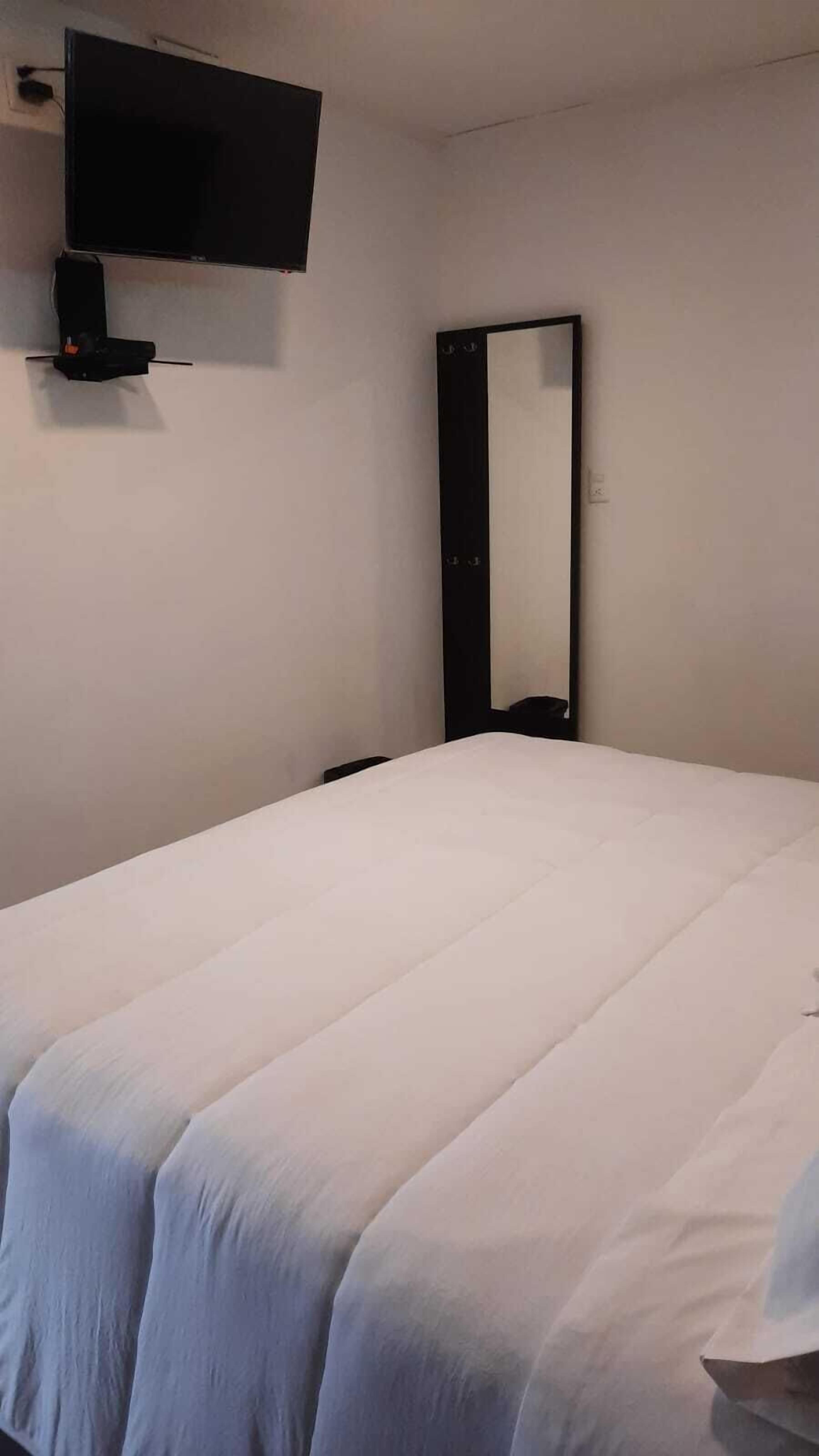 Quarto de hotel com uma cama, televisão de tela plana na parede e um espelho grande.
