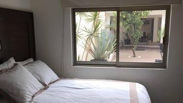 Un dormitorio con un ventanal grande, una cama con ropa de cama blanca y vistas al exterior.