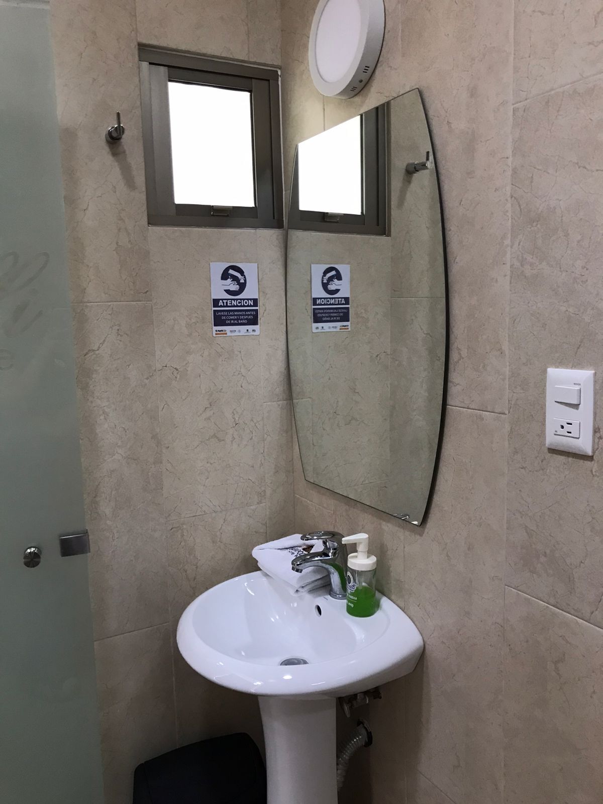 A bathroom with a white sink, a mirror, and two signs on the wall.