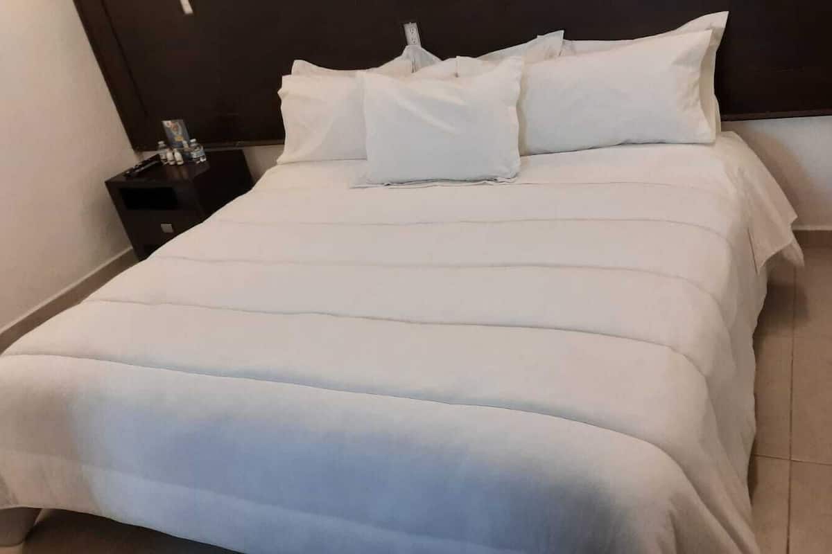 A neatly made bed with white linens, a dark headboard, and a small bedside table with a lamp.