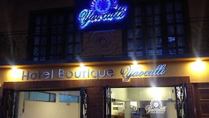 Das Hotel Boutique Yacalli mit leuchtendem Neon-Schild, großen Glasüren und einem einsehbaren Innenbereich mit Rezeption.
