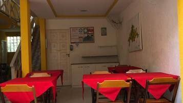 Un comedor con mesas y sillas, una cocina al fondo, y una escalera que lleva a un nivel superior.