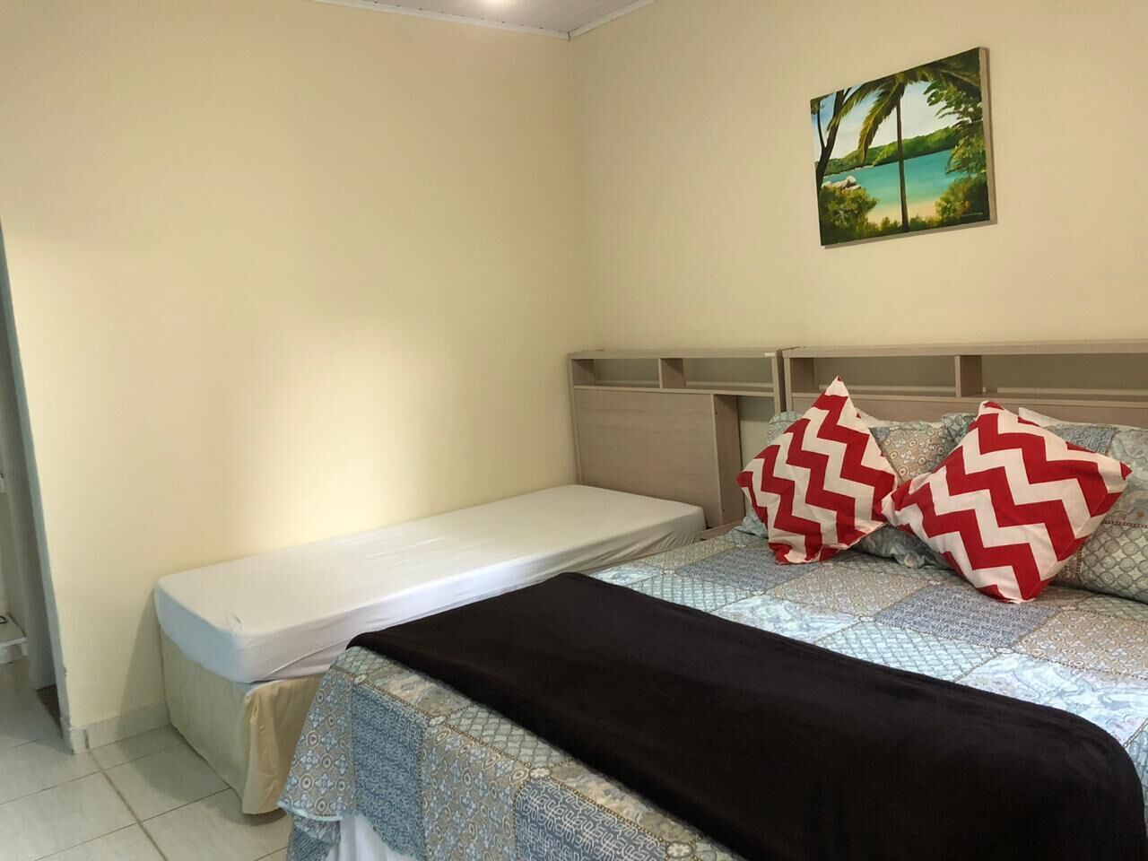 Quarto com uma cama de solteiro, cabeceira e um quadro na parede.