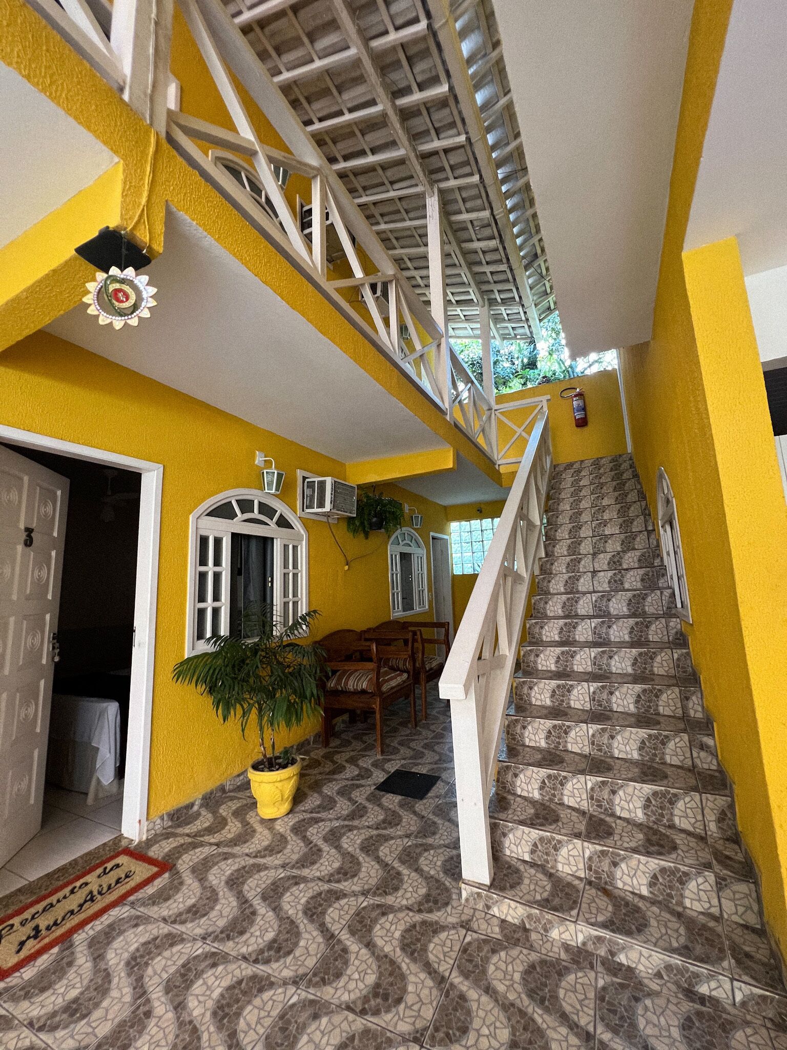 A staircase with white railings leading to a second floor, a potted plant, and a door with a mat.