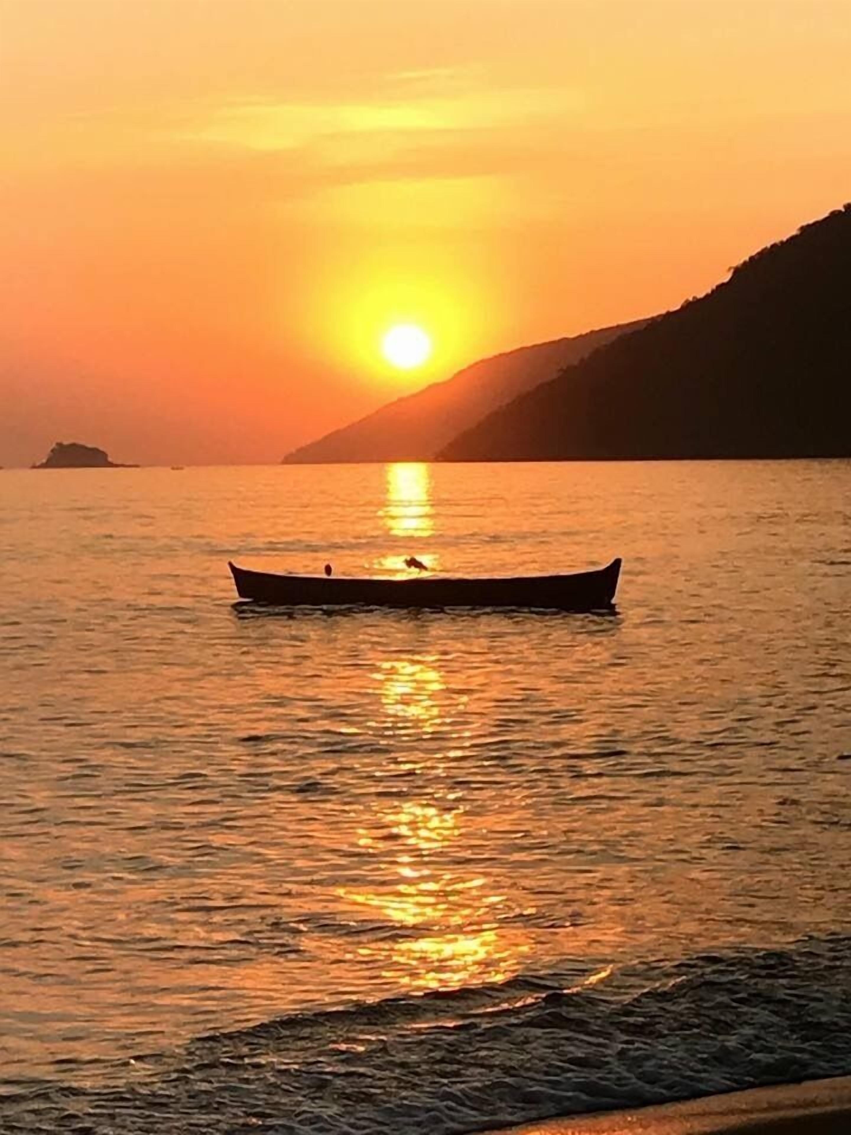 A sunset over calm water with a boat in the foreground.