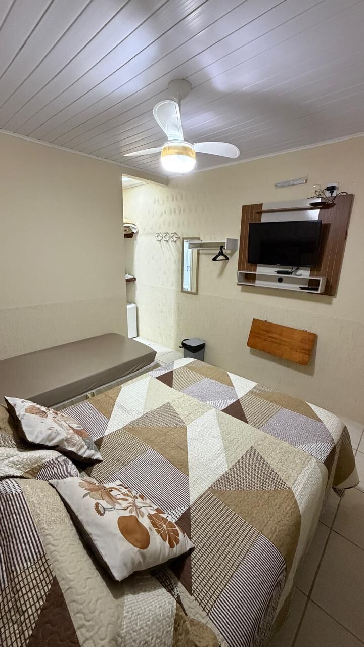 A bedroom with a bed, a ceiling fan, a TV, and a small bedside table.