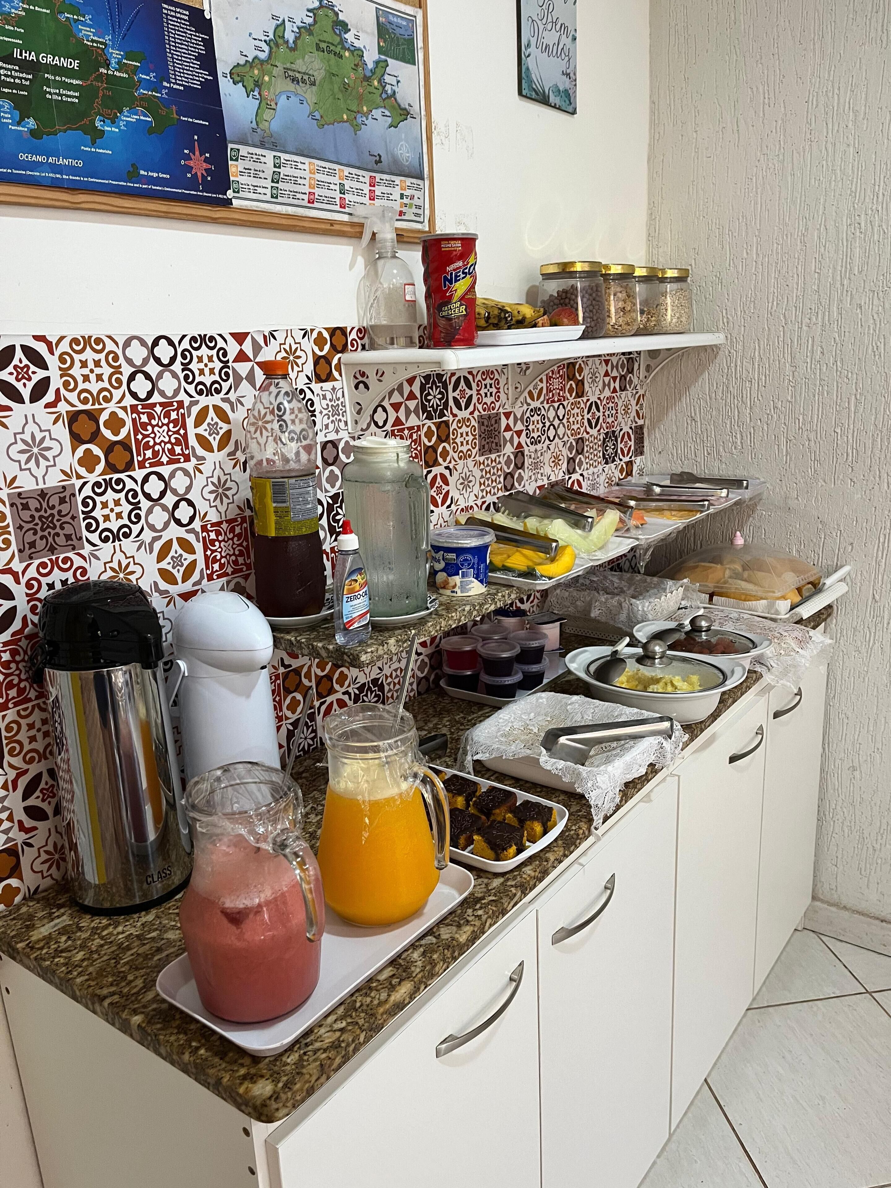 Eine Küchenarbeitsplatte mit verschiedenen Lebensmitteln und Küchenutensilien, darunter eine Thermoskanne, eine Saftflasche und eine Dose Nescafé.