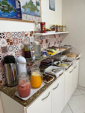 Un plan de travail de cuisine avec divers aliments et ustensiles, notamment un thermos, une bouteille de jus et une boîte de Nescafé.