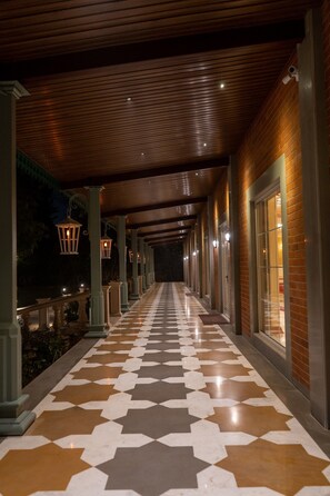 Un corridoio coperto con pavimento decorato, travi in legno a soffitto e luci a parete.