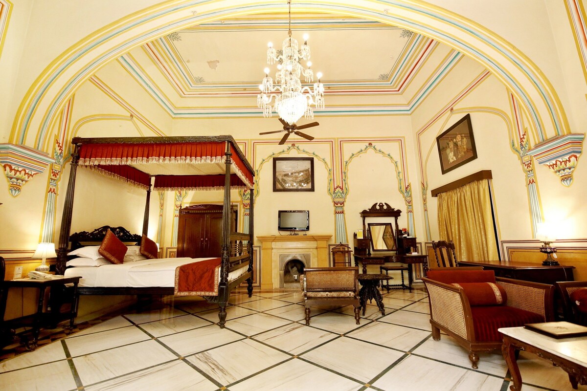 Ein traditionelles Bett mit Baldachin, ein Kamin, ein Fernseher und klassische Möbel in einem stilvoll eingerichteten Zimmer.