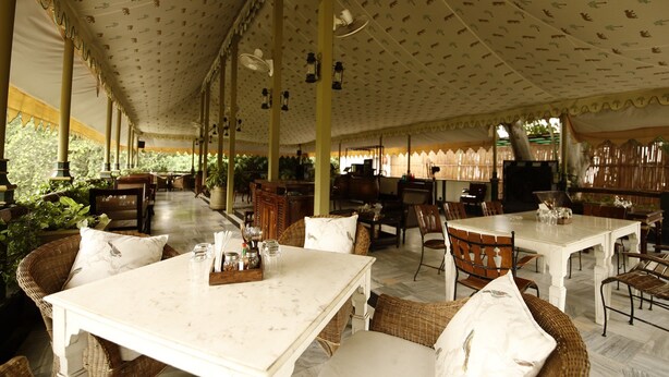 A covered outdoor dining area with tables and chairs, patterned ceiling, and natural light. - Narain Niwas Palace (Jaipur)