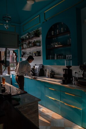 Una cucina con mobili color petrolio, una macchina per caffè e una persona che sta preparando qualcosa.