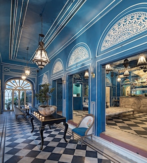 Vestíbulo de hotel con suelo de cuadros, paredes azules, diseños ornamentales en el techo y candelabros.