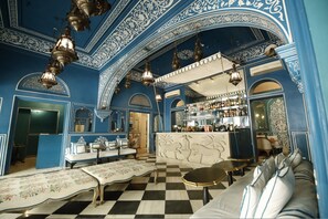 A bar area with a checkered floor, ornate blue and white wall designs, and hanging lantern-style lights.
