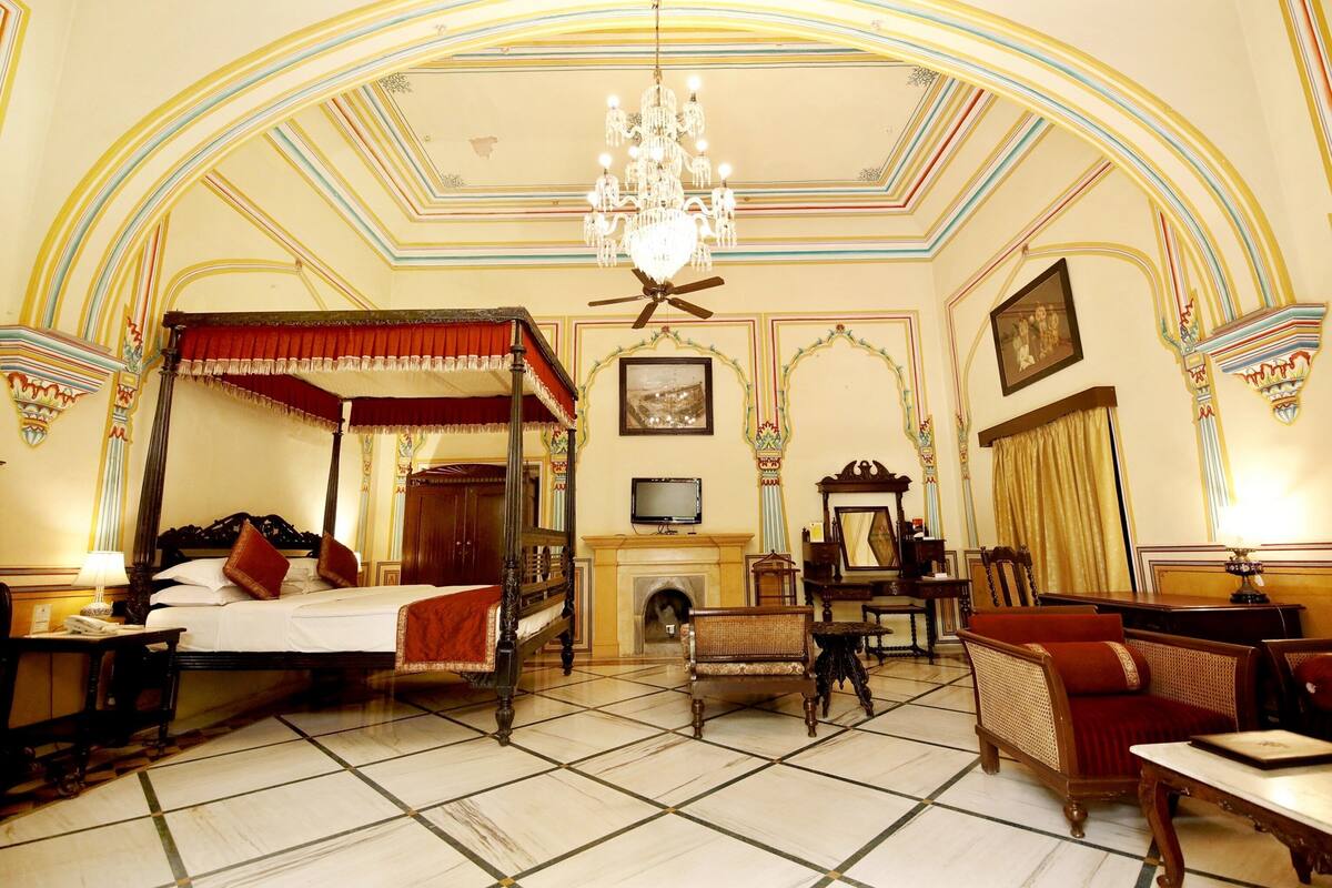 Un lit à baldaquin traditionnel, une cheminée, un téléviseur et des meubles classiques dans une pièce élégamment décorée.