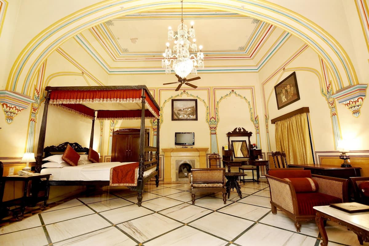 Un lit à baldaquin traditionnel, une cheminée, un téléviseur et des meubles classiques dans une pièce élégamment décorée.