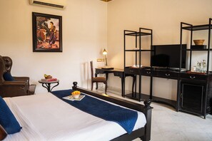 Ein Hotelzimmer mit einem Bett, einem Schreibtisch mit Fernseher, einem Sessel, einem kleinen Tisch mit Lampe und einem Bild an der Wand.