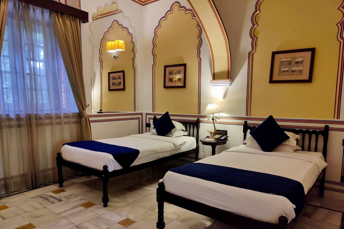 Une chambre d’hôtel avec deux lits, une table de chevet, une lampe et des tableaux encadrés aux murs.