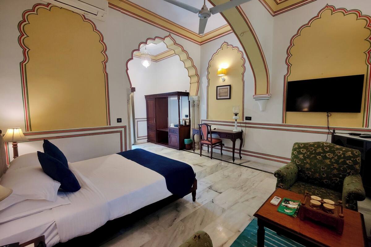 Une chambre d’hôtel équipée d’un lit, d’un bureau, d’une chaise, d’une télévision et d’un ventilateur de plafond.