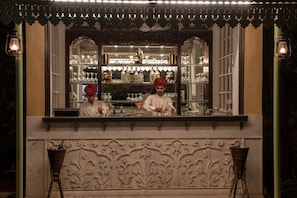 A bar with shelves of bottles and glasses, a decorative ceiling, and a carved wall. - Narain Niwas Palace (Jaipur)