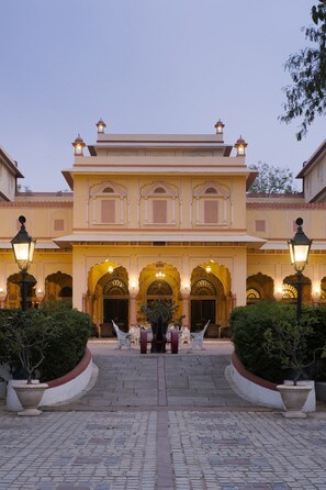 A grand building with multiple arches and a central entrance, surrounded by potted plants and a paved walkway. - Narain Niwas Palace (Jaipur)