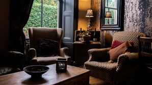 Una habitació acollidora amb dues butaques estampades, una taula de fusta amb un bol, una làmpada i vista a vegetació a través d'una finestra.