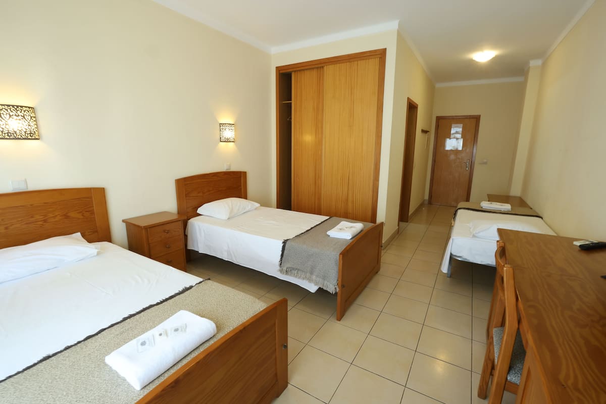 A hotel room with two beds, a wooden desk, a wardrobe, and a bathroom door.