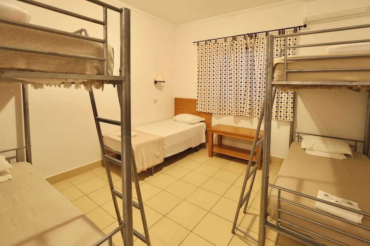 A dormitory room with bunk beds, a wooden desk, and a window with a polka dot curtain.