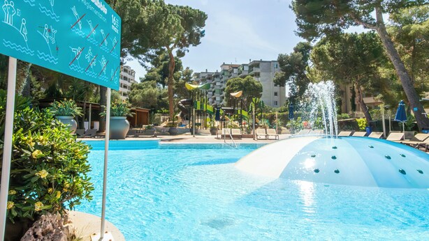 Una piscina con tobogán de agua, sillas de descanso y un cartel con indicaciones para nadar.