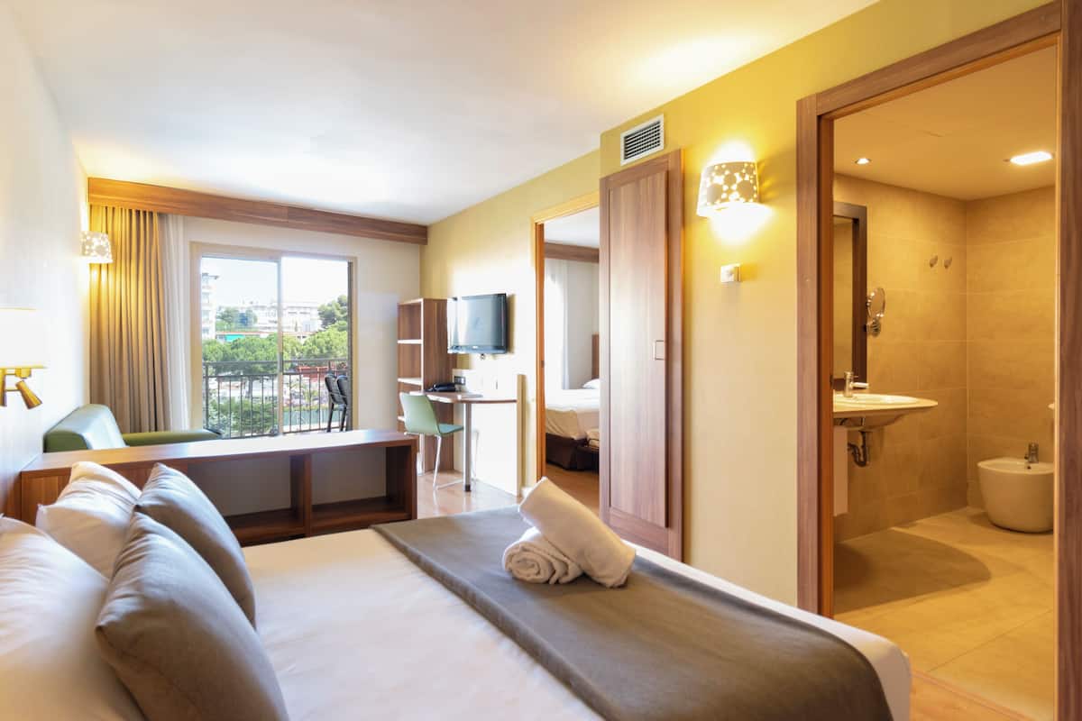 A hotel room with a bed, a desk, a TV, a bathroom, and a view of the outside.