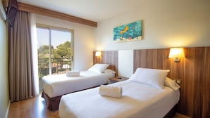 Una habitación de hotel con dos camas, un ventanal con cortinas, un cuadro de una escena marina y un cabecero de madera.