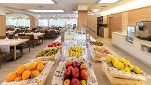 Cafetería con mesas y sillas, una exposición de frutas y una escalera que sube a un nivel superior.