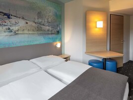 Habitación de hotel con cama, mesita de noche, lámpara de pared, espejo y un cuadro con una escena de playa.