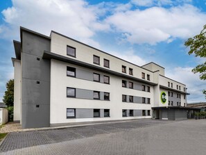 Un hotel moderno con techo plano, múltiples ventanas y una zona de estacionamiento.