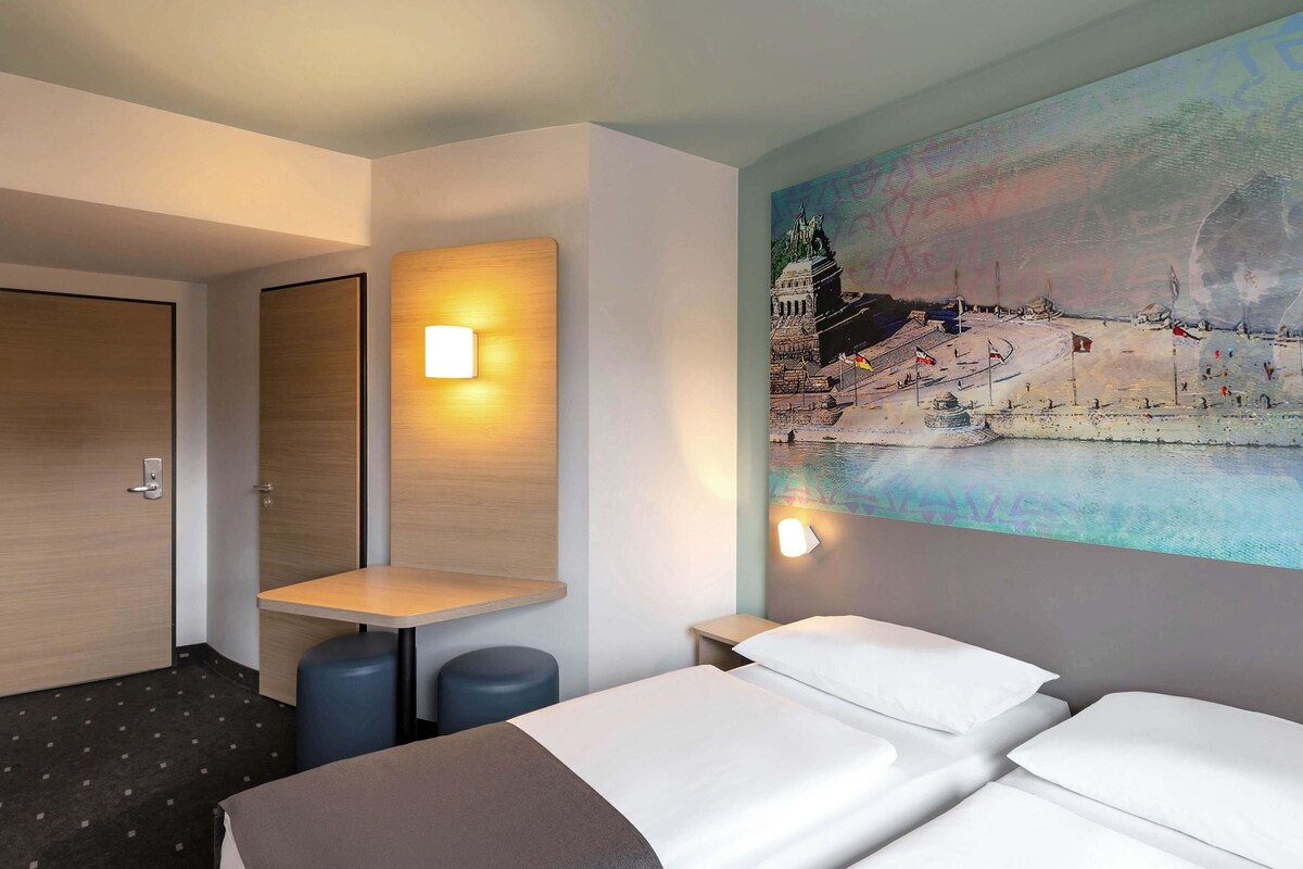Una habitación de hotel con dos camas, una mesita y una lámpara fijada a la pared.