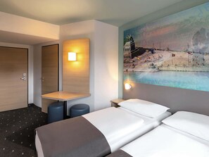Una habitación de hotel con dos camas, una mesita y una lámpara fijada a la pared.