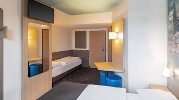 Ein kleines Hotelzimmer mit einem Bett, einem Schreibtisch, einem Spiegel, einem Waschbecken und einer Tür.