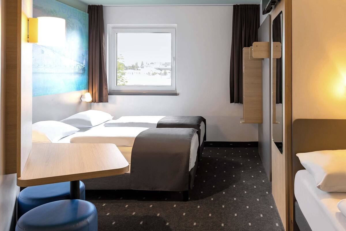 A hotel room with two beds, a small table, and a window with a view.