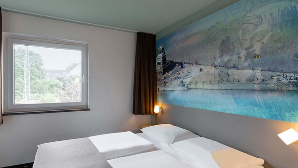 A hotel room with a bed, a window, a painting, and a nightstand. - B&B HOTEL Koblenz-City (Koblenz)