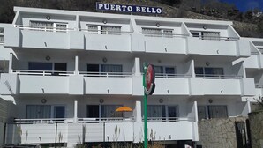 Un hotel de varios pisos llamado Puerto Bello con balcones y un muro de piedra al frente.