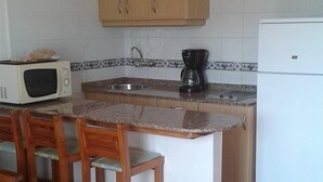 Una cocina con armarios de madera, microondas, cafetera y refrigerador.