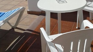 Un patio con sillas de plástico blanco y una mesa redonda, suelo de baldosas y pared blanca.