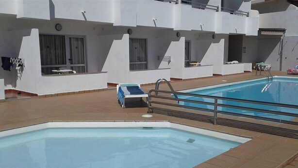 Una piscina con un sillón de tomar el sol y una pequeña mesa, rodeada de muros blancos y un suelo de baldosas.
