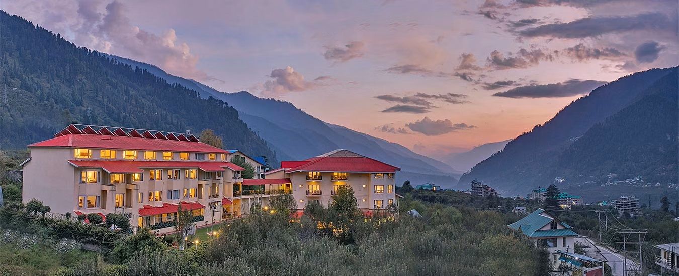 A hotel with multiple buildings, red roofs, and a mountainous backdrop.