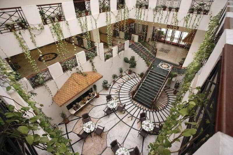 A multi-level atrium with a central spiral staircase, surrounded by tables and chairs, and adorned with hanging plants.