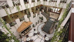 Un atrium à plusieurs niveaux, doté d’un escalier en colimaçon central, entouré de tables et de chaises, et agrémenté de plantes suspendues.