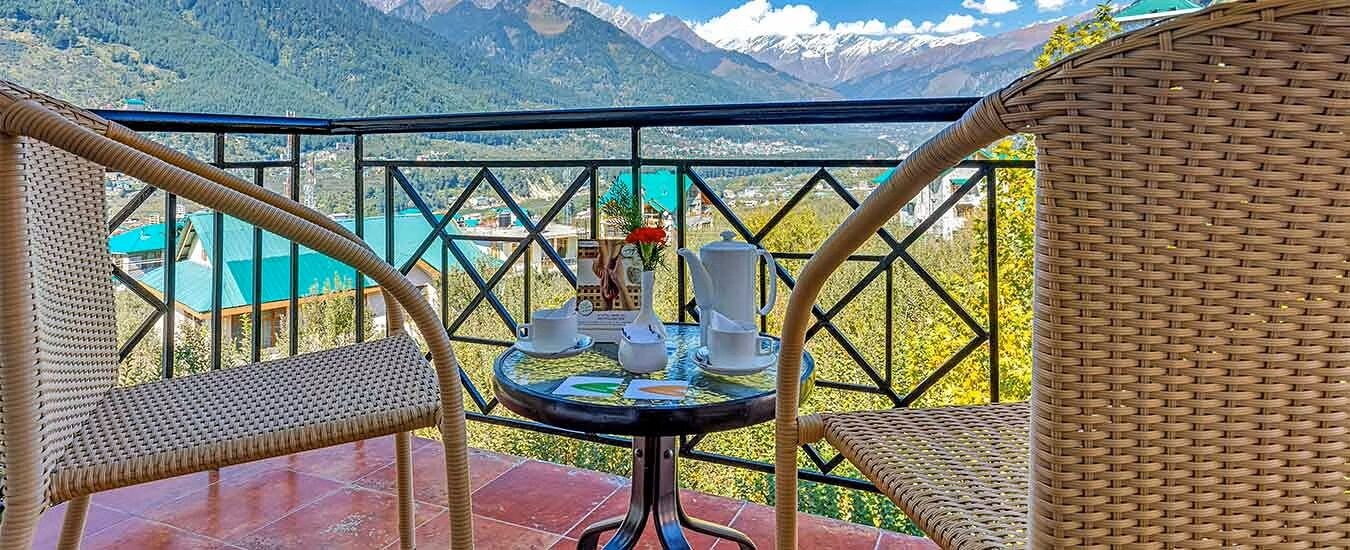A balcony with wicker chairs, a table with a vase and teacups, and a mountain view.